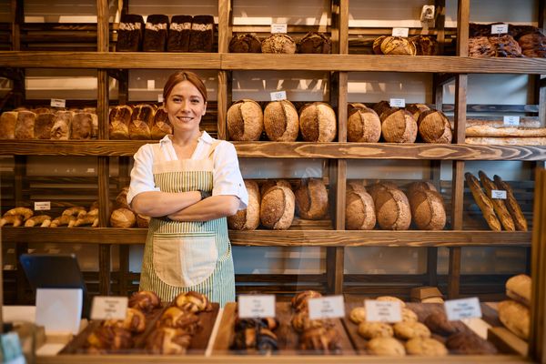 Smiling baker standing in front of shelves filled with various breads.