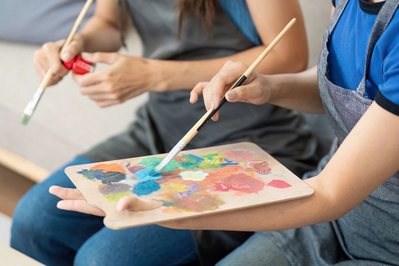 Two women joyfully painting together, sharing colors and laughter in a cozy indoor atmosphere, highlighting their bond and creativity.