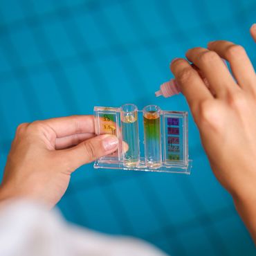 Person testing pool water with a chemical test kit near a swimming pool.