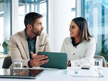 Two professionals discussing work with a tablet in a modern office.