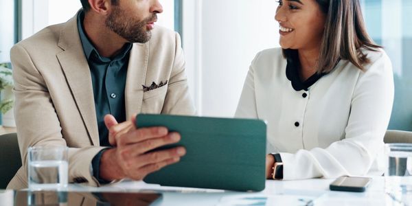 Two professionals discussing work over a tablet in a modern office.