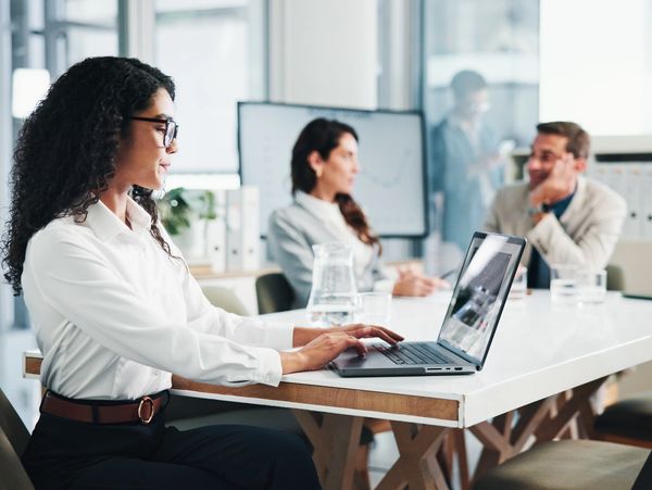 A woman in glasses works on a laptop during a business meeting.