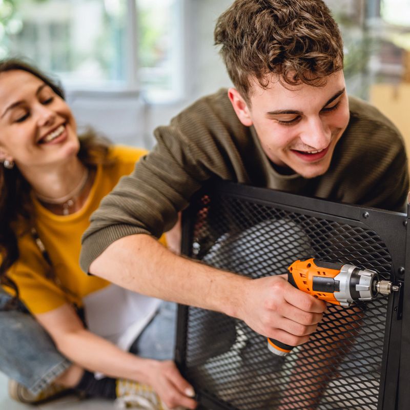 Adult couple have fun and use electric drill for assembling table at new apartment. Concept of family, relocation and manual work