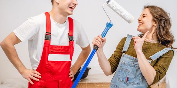 A smiling couple in overalls enjoying painting together indoors.