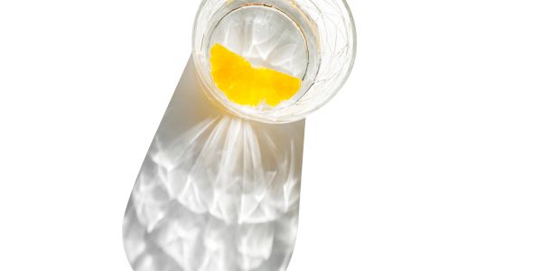Glass of water with orange slice casting shadow.