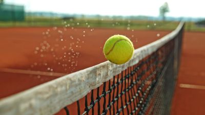 Tennis ball bouncing on the net of a clay court.