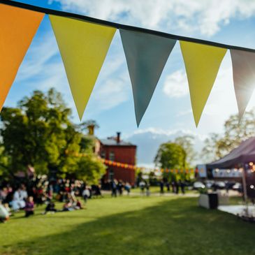 Colorful triangular flags hang above a sunny outdoor gathering.
