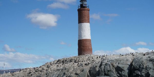 Leuchtturm auf felsiger Insel unter blauem Himmel.