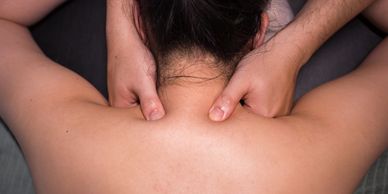 Person receiving a neck massage with fingers pressing shoulder muscles.
