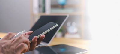 Person using smartphone with tablet and laptop on desk in background.