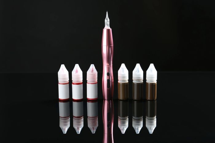 Tattoo machine with ink bottles in red and brown shades on reflective surface.