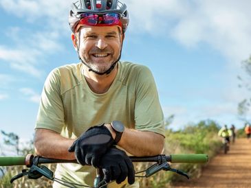 Smiling man with a bike helmet resting on his bicycle.