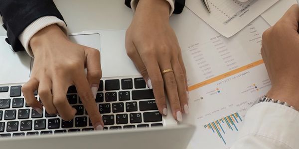Manos trabajando en una computadora portátil con documentos.