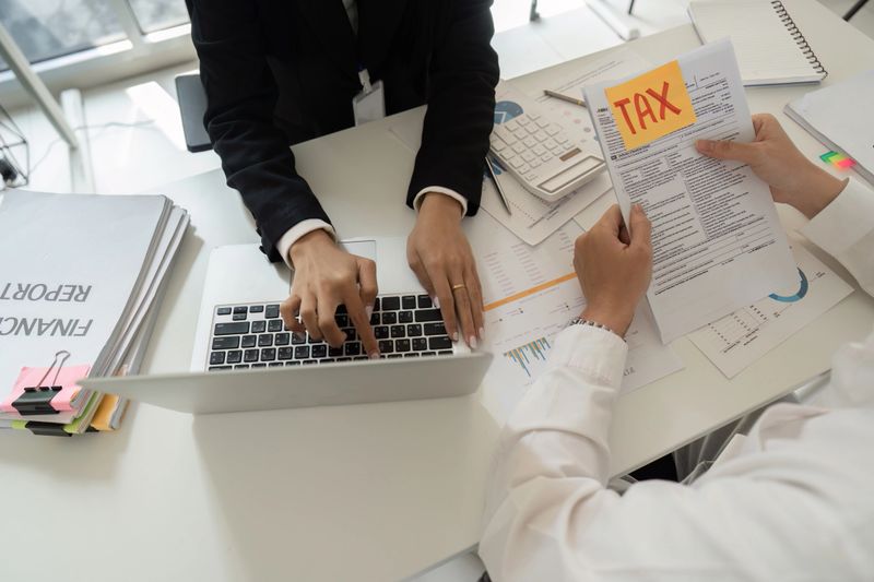 A tax consultant helps a client with financial reports, focusing on tax documents and calculations in a professional setting.