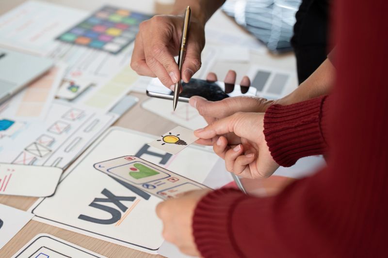 Colleagues collaborate on UX/UI design concepts, sharing ideas and taking notes while reviewing wireframes and prototypes in a creative workspace.