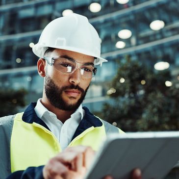 Engineer in safety gear using a tablet at a construction site.