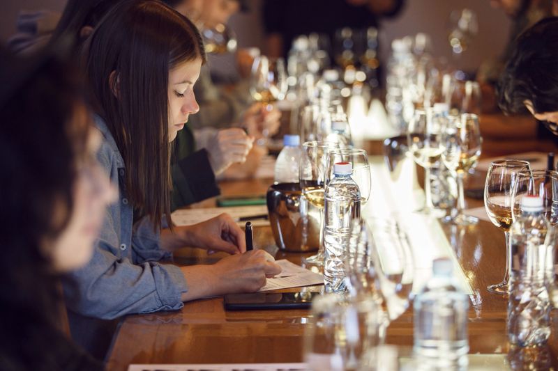 Focused female sommelier is jotting down her observations on a degustation card as she participates in a wine tasting event.