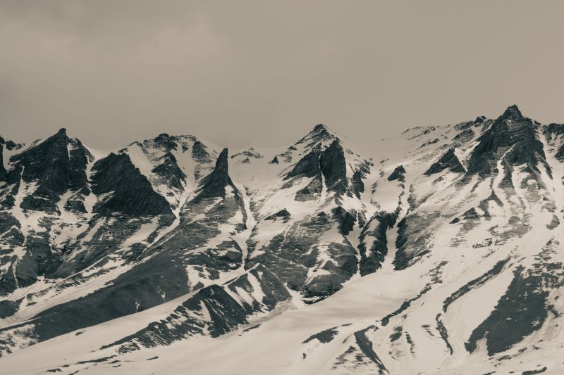 A powerful monochrome capture of the jagged Caucasus peaks in winter, where snow clings to steep cliffs and dramatic ridges slice through the sky. The stark contrasts between dark rock and bright snow emphasize the raw, untamed beauty of this alpine wilderness. This image evokes a sense of timeless solitude and natural grandeur. Georgia