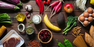 A variety of fresh fruits, vegetables, nuts, and other healthy foods arranged on a wooden surface.