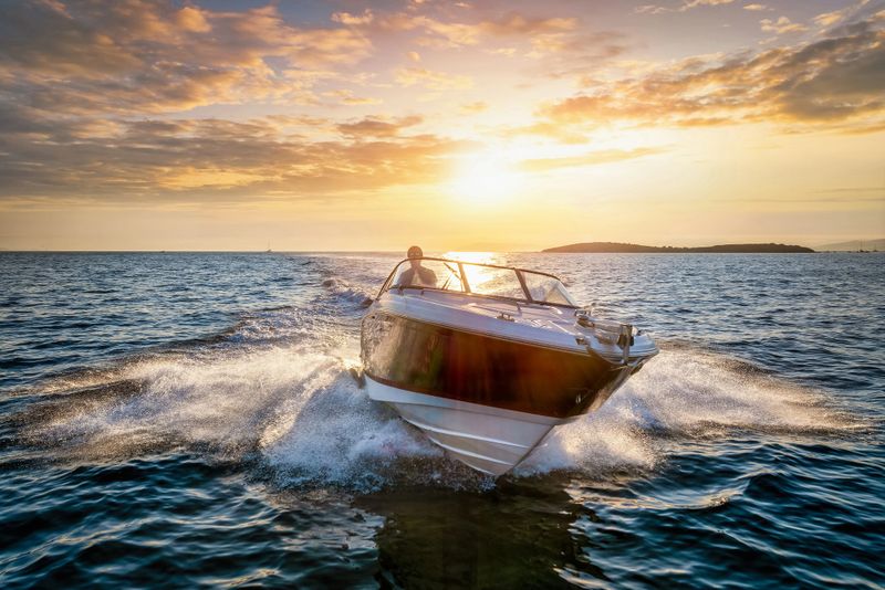 Aerial front view of a motor boat cruising with speed over the ocean during sunset time with copy space