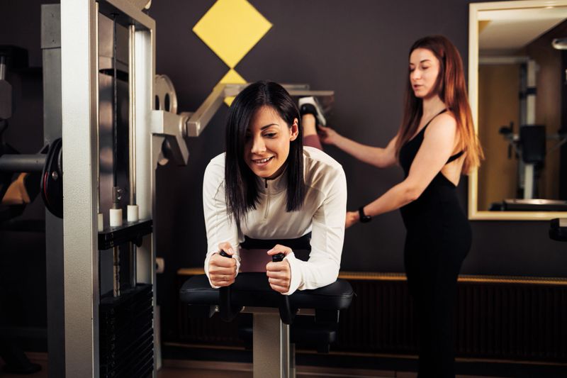 A fitness trainer provides guidance to a gym client using gym equipment for exercises in a modern fitness center environment. The image showcases teamwork and dedication during a workout session.