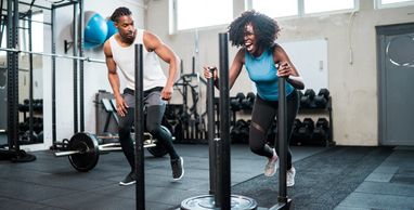 Two people pushing weighted sleds in a gym with determined expressions.