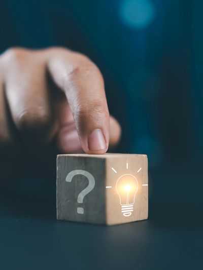 Finger touching a wooden cube with question mark and lightbulb icons.
