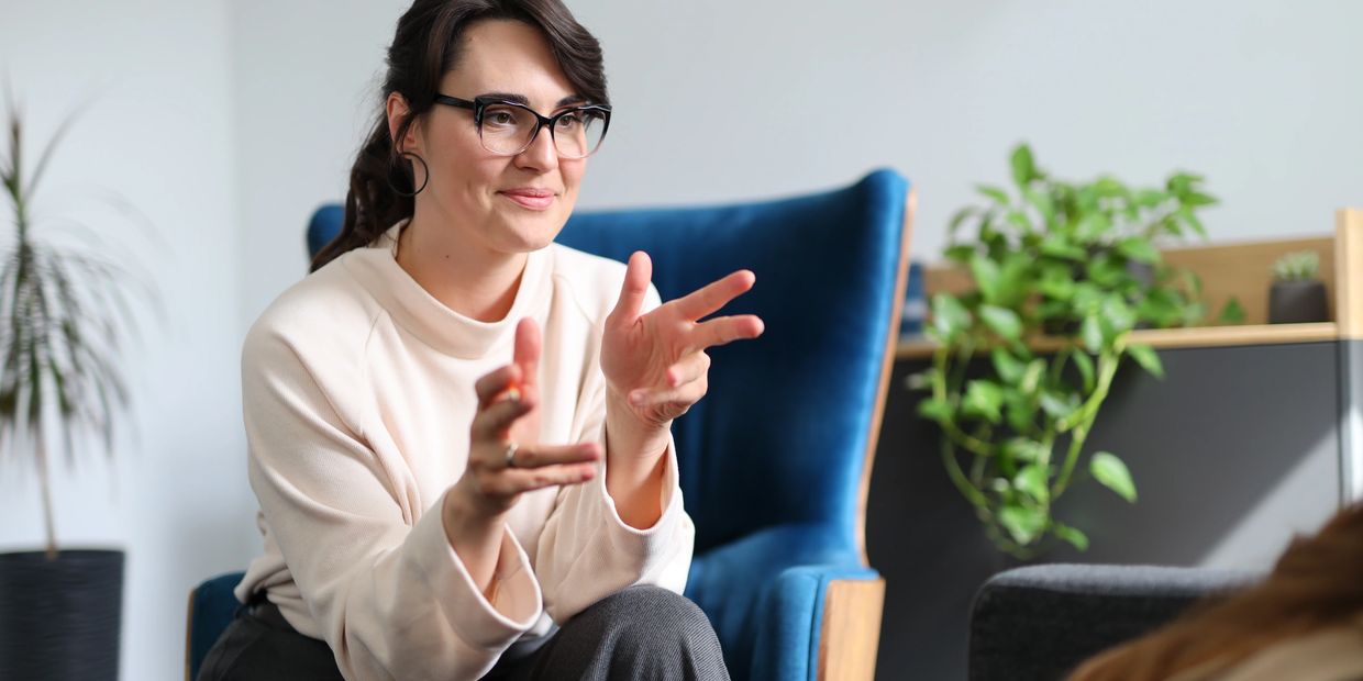 Woman in glasses engaged in conversation, sitting on a blue chair.