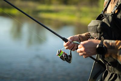 Person fishing with a rod near a calm body of water.