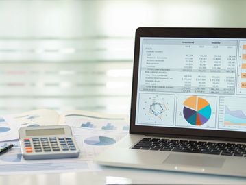 Laptop displaying graphs with calculator and papers.