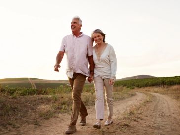 Elderly couple walking hand in hand on a dirt path.