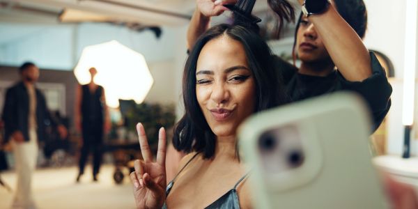 Femme prenant un selfie en faisant un signe de paix pendant qu'elle se fait coiffer.