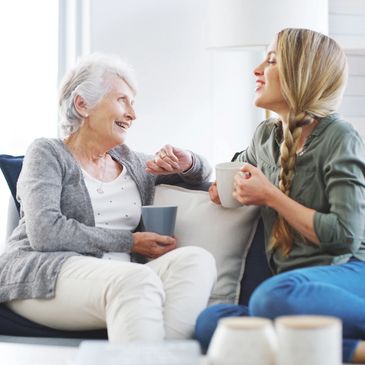 An elderly woman and a young woman happily chatting over coffee on a couch.