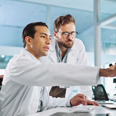 Two scientists in lab coats discussing data on a computer.