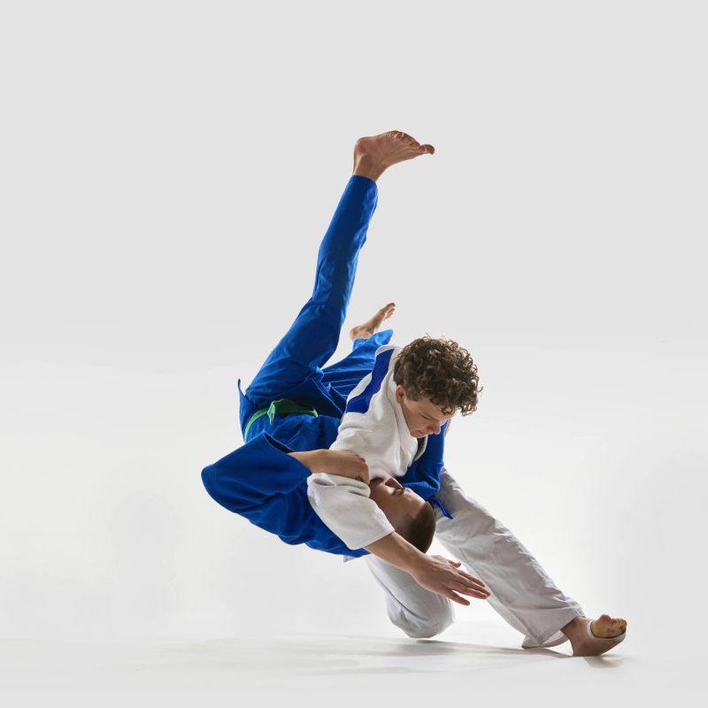 Flawless takedown in motion, fighter in white executing classic over-the-shoulder throw as blue gi opponent is launched into air, highlighting mastery. Concept of championship, victory, competition.