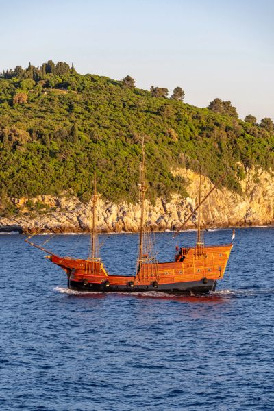 Wooden sailboat near a rocky green coastline.