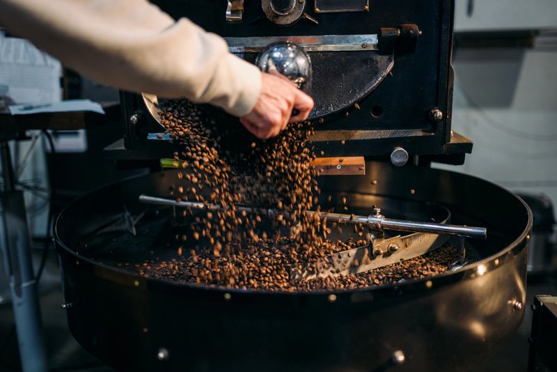 A local urban coffee roasting business roasts singing origin coffee beans for cafes and shops.  A Caucasian man operates the machine and tends to the beans during the roast process.  Shot in Portland, Oregon, USA.