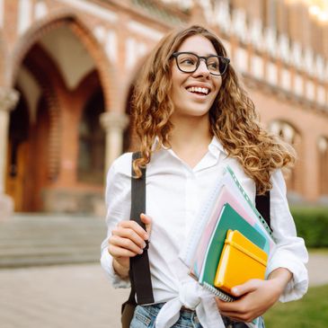 Smiling student holding notebooks outside a college building.