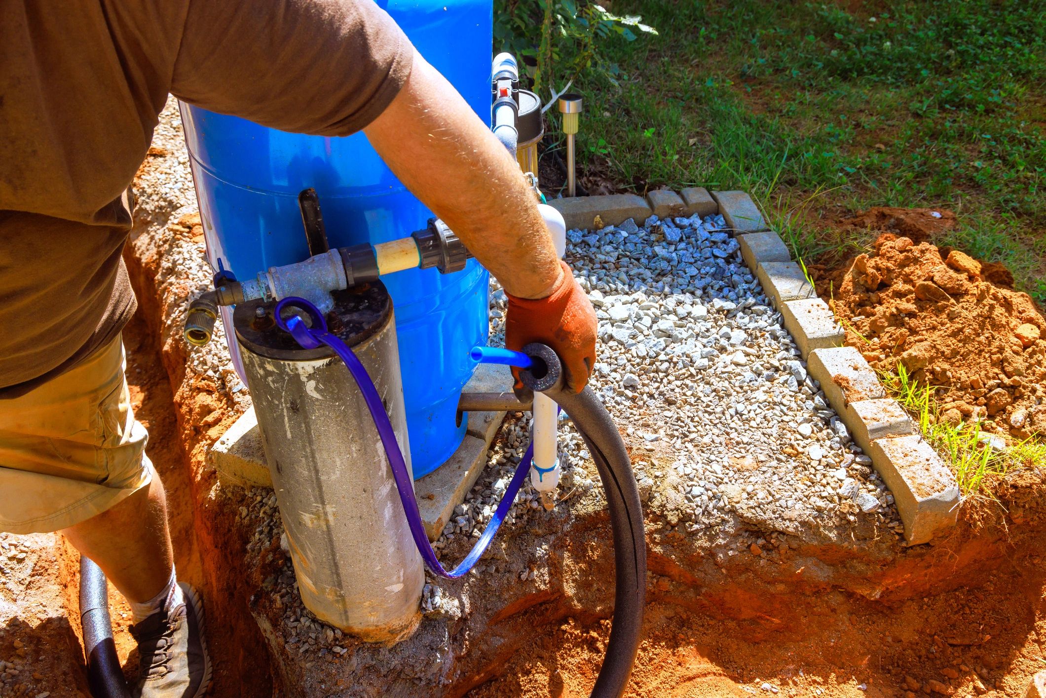 Person working on water pump system outdoors with gravel around.