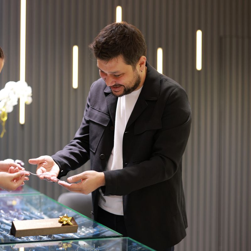Elegant middle age businessman choosing and buying his new expensive watch. Beautiful youg female seller helps him to make good decision. Fashion style and elegance concept.