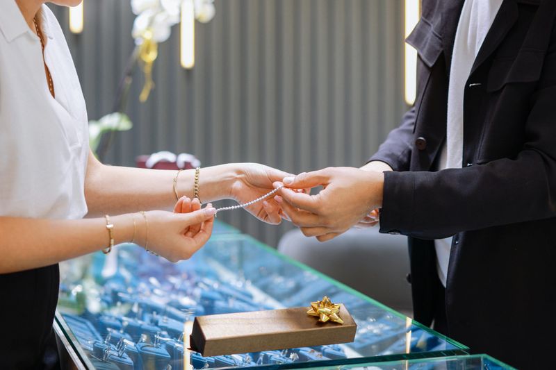 Elegant middle age businessman choosing and buying his new expensive watch. Beautiful youg female seller helps him to make good decision. Fashion style and elegance concept.