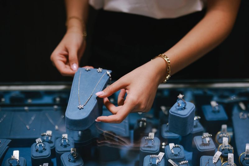 Expensive necklace and earring set on display. A well-dressed saleswoman working in a jewelry store. She is holding up three pearl necklaces on a display stand.