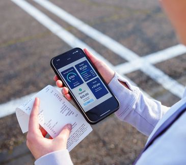 Person checks a fitness app on phone while holding a printed receipt outdoors.