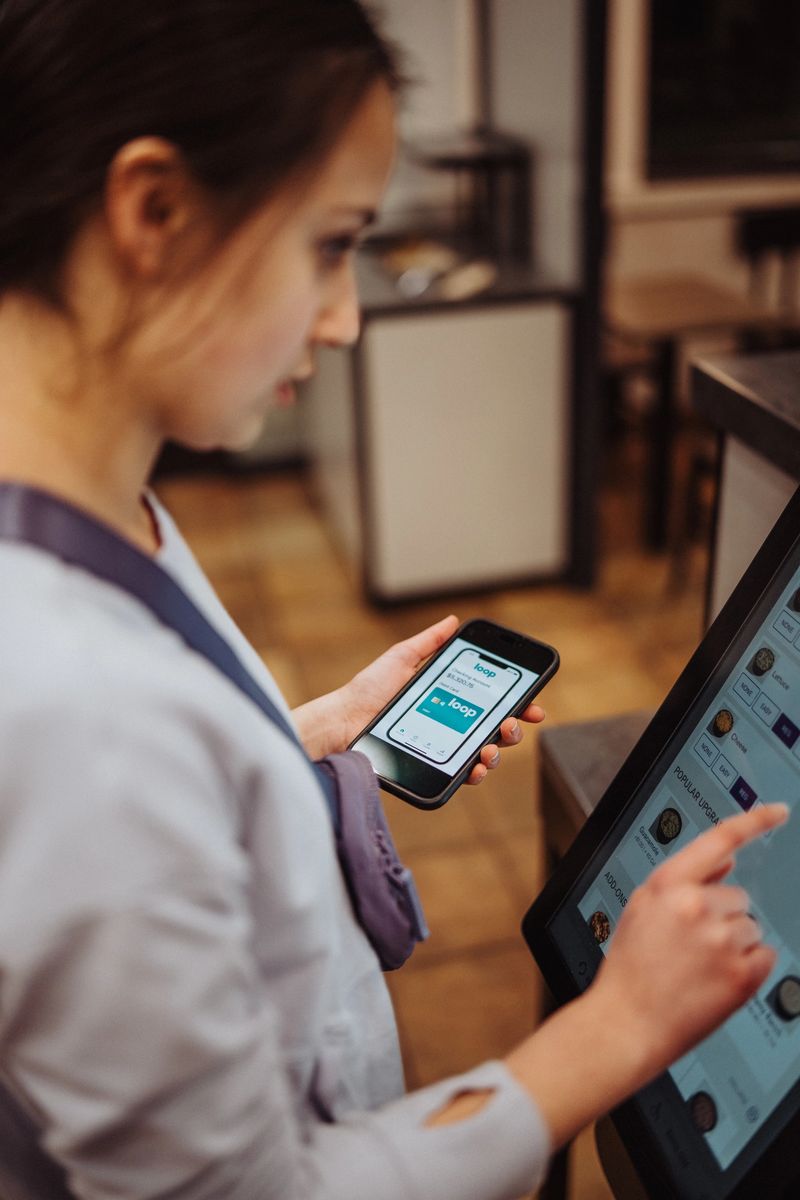 Cropped view of an Eurasian teenage girl ordering a meal using a  self-service kiosk with touch screen, with selective focus on her smart phone which is opened to a digital wallet app for convenient contactless payment.