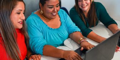 Three women smiling and working together on a laptop.