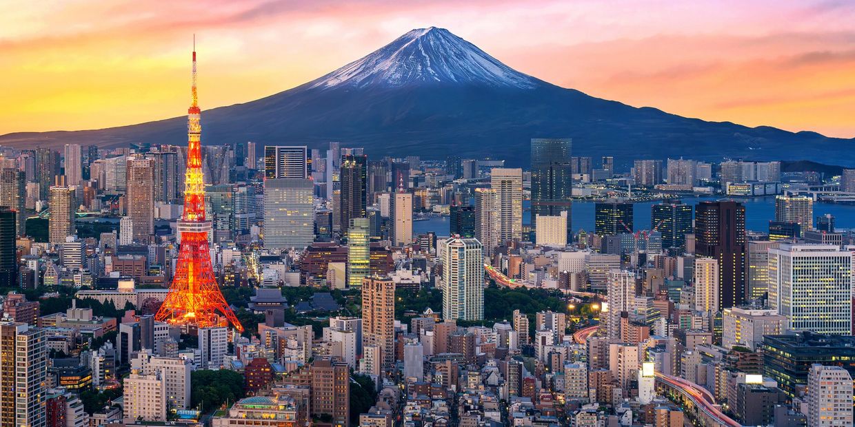 Cityscape with illuminated tower and mountain backdrop at sunset.