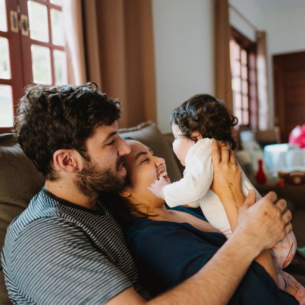 A joyful family moment with parents and baby on a couch.