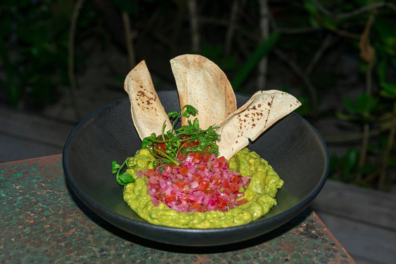 A fresh serving of creamy guacamole accompanied by crispy nachos and topped with vibrant red onion slices. A flavorful and colorful appetizer perfect for sharing.