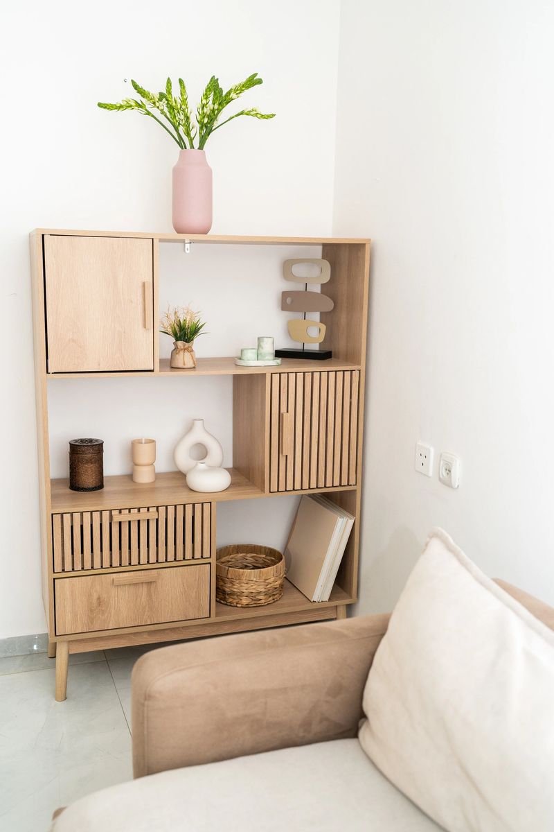 A wooden shelf in a minimalistic interior displays various decorative items and plants. Soft lighting accentuates the natural wood texture and creates a welcoming atmosphere.