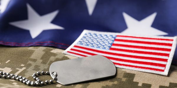 Military dog tags with American flag patch and folded flag background.